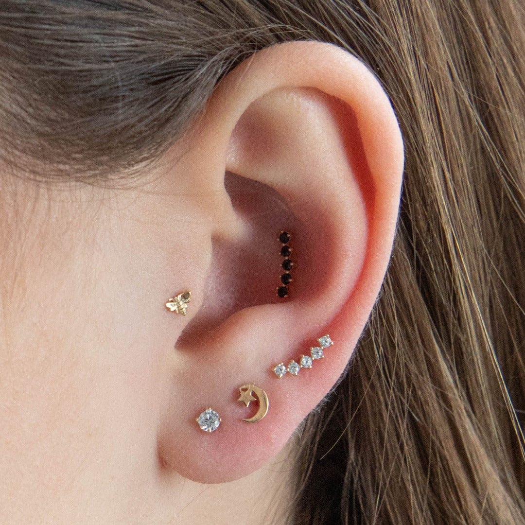 14 Carat Yellow Gold Tiny Bee Labret Piercing shown in the tragus position on a models ear styled with midnight inner conch and 3 lobe piercings in solid gold