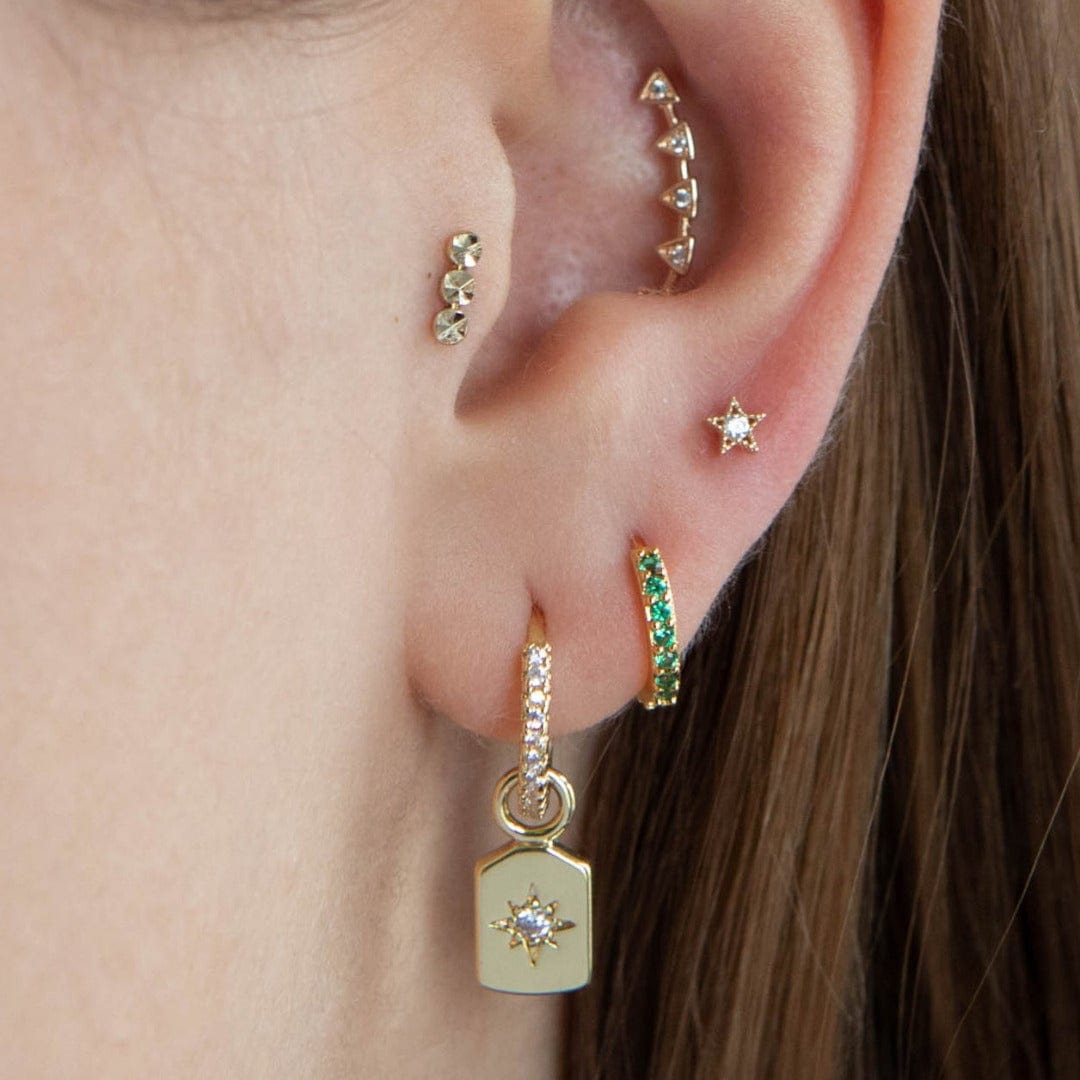 14 carat gold disco thread labret piercing shown in the tragus position of the ear, shown in yellow gold. The model also wears an inner conch barbell and 3 lobe earrings all in gold 