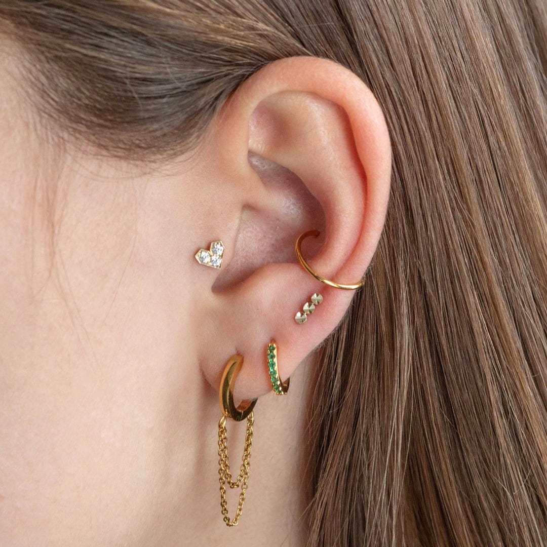 14 carat gold full heart with 3 round clear crystals, shown in the tragus position of the model. The model wears a gold conch ring and 3 lobe piercings.