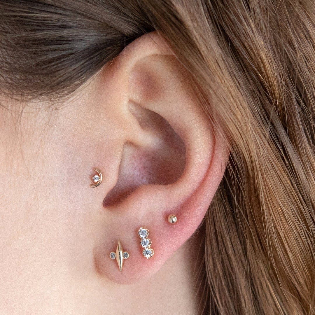 14 Carat Solid Gold Sunrise Arc Labret Stud with 1 clear circular CZ gems shown in the tragus position on the model. The model wears 3 lobe piercings