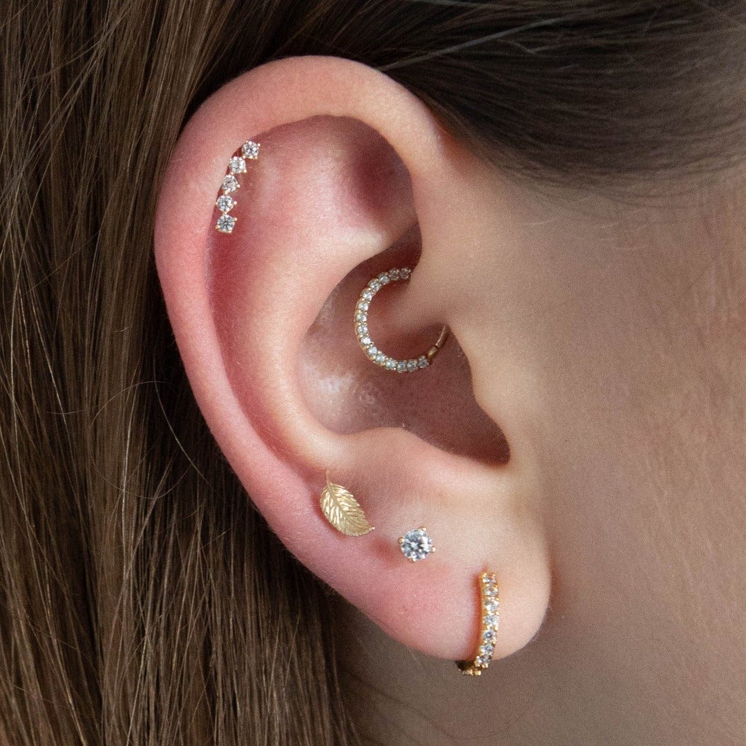 infinity daith hoop, a 14 carat solid gold classic circular hoop with ring of cubic zirconia shown in the daith position on ear model. The model also wears a helix earring and 3 gold lobe piercings