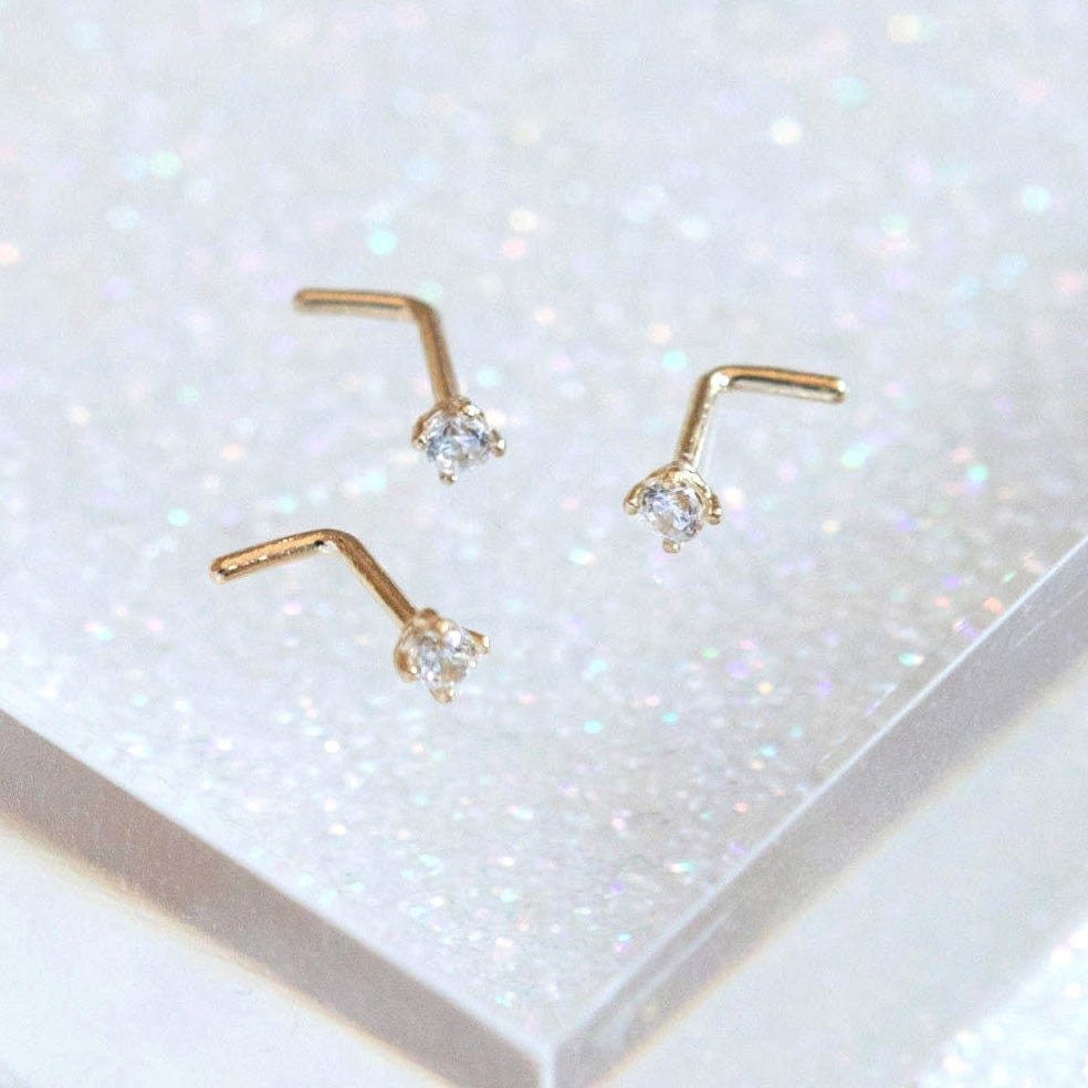 14 Carat Gold Solitaire Nose Stud with 1 single tiny clear CZ gems shown on glittery background
