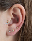 14 Carat gold flat moon and star thread labret piercing shown on the model in the second lobe position. The model has two further lobe piercings, a midnight inner conch crawler and flower bud tragus all in yellow gold