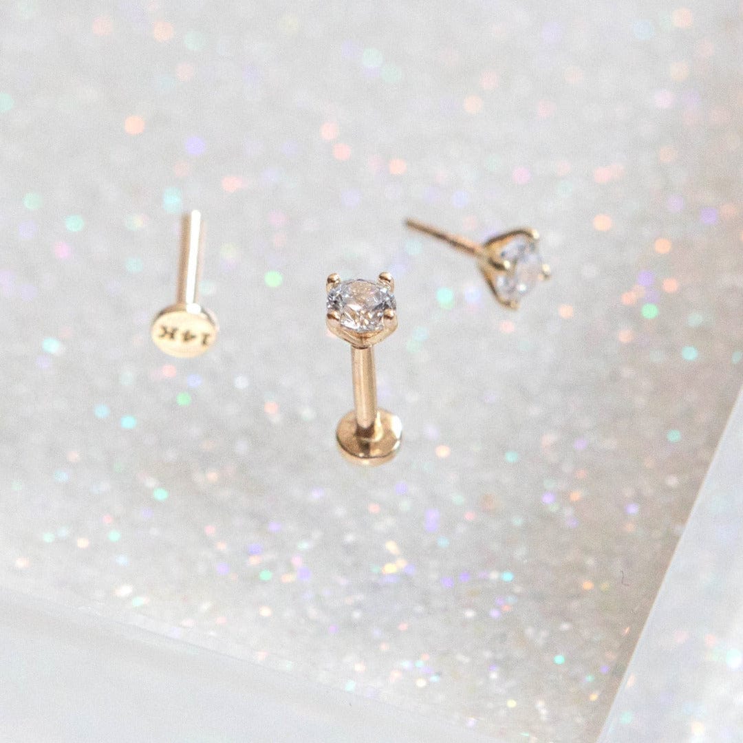 14K Solid Gold Solitaire Labret Piercing with a single CZ crystal shown on glittery background with a further piercing which has been laid flat.