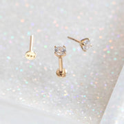 14K Solid Gold Solitaire Labret Piercing with a single CZ crystal shown on glittery background with a further piercing which has been laid flat.