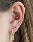 14K Solid Gold Solitaire Labret Piercing with a single CZ crystal shown in the tragus position of the model. The model wears 3 further lobe piercings and an inner conch crawler