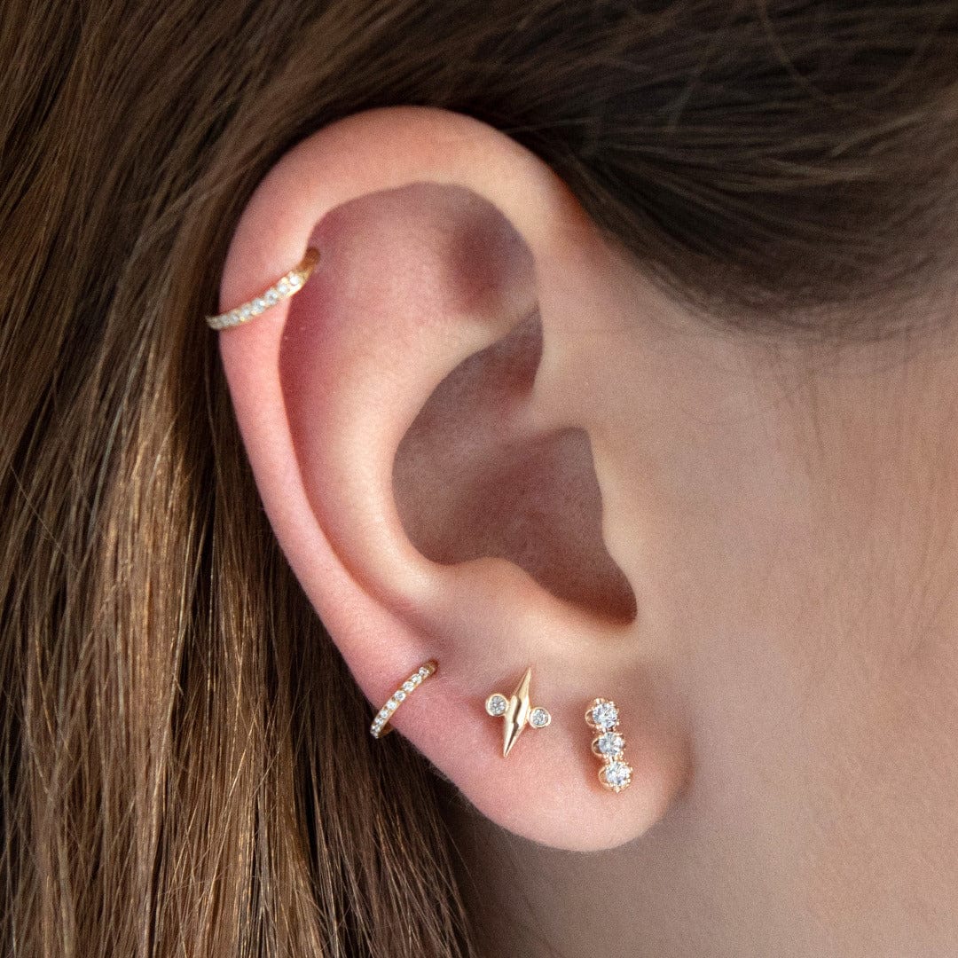 4K Solid Gold Tryptic Barbell with 3 large clear CZ gems in a trellis mount shown in the first lobe position of the model. The model wears 2 further lobe piercing and a crystal helix hoop